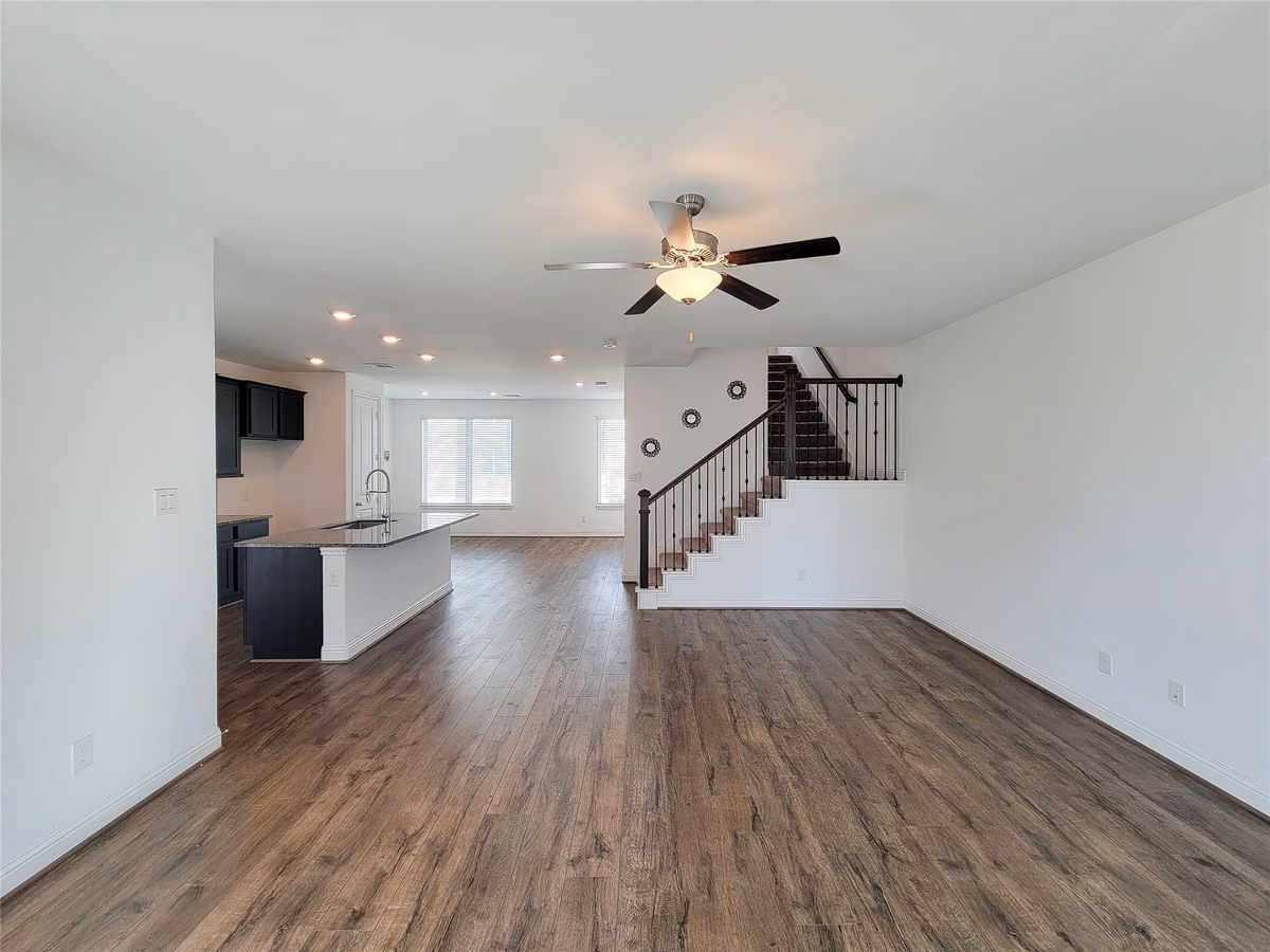 Spacious open concept living area featuring elegant wood flooring, a modern kitchen with an island, and a stylish staircase leading to the upper level.