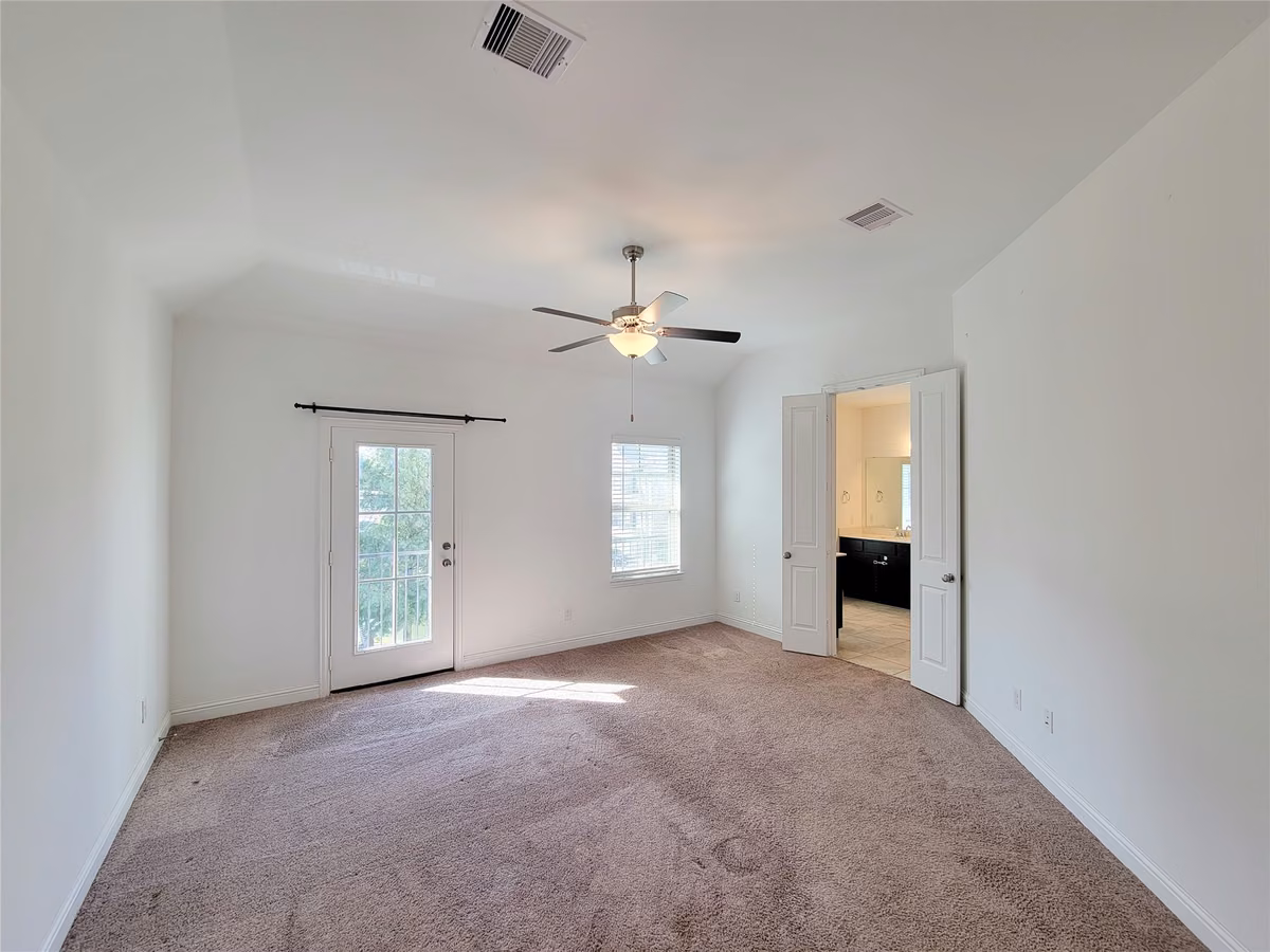 Spacious bedroom with plush carpeting, abundant natural light, and access to a private balcony through elegant French doors.