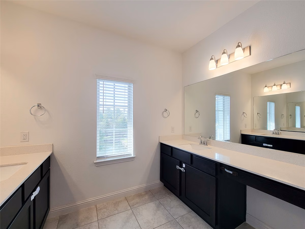 Spacious bathroom featuring dual sinks with modern fixtures, sleek dark cabinetry, and a large mirror, offering ample light and elegance.