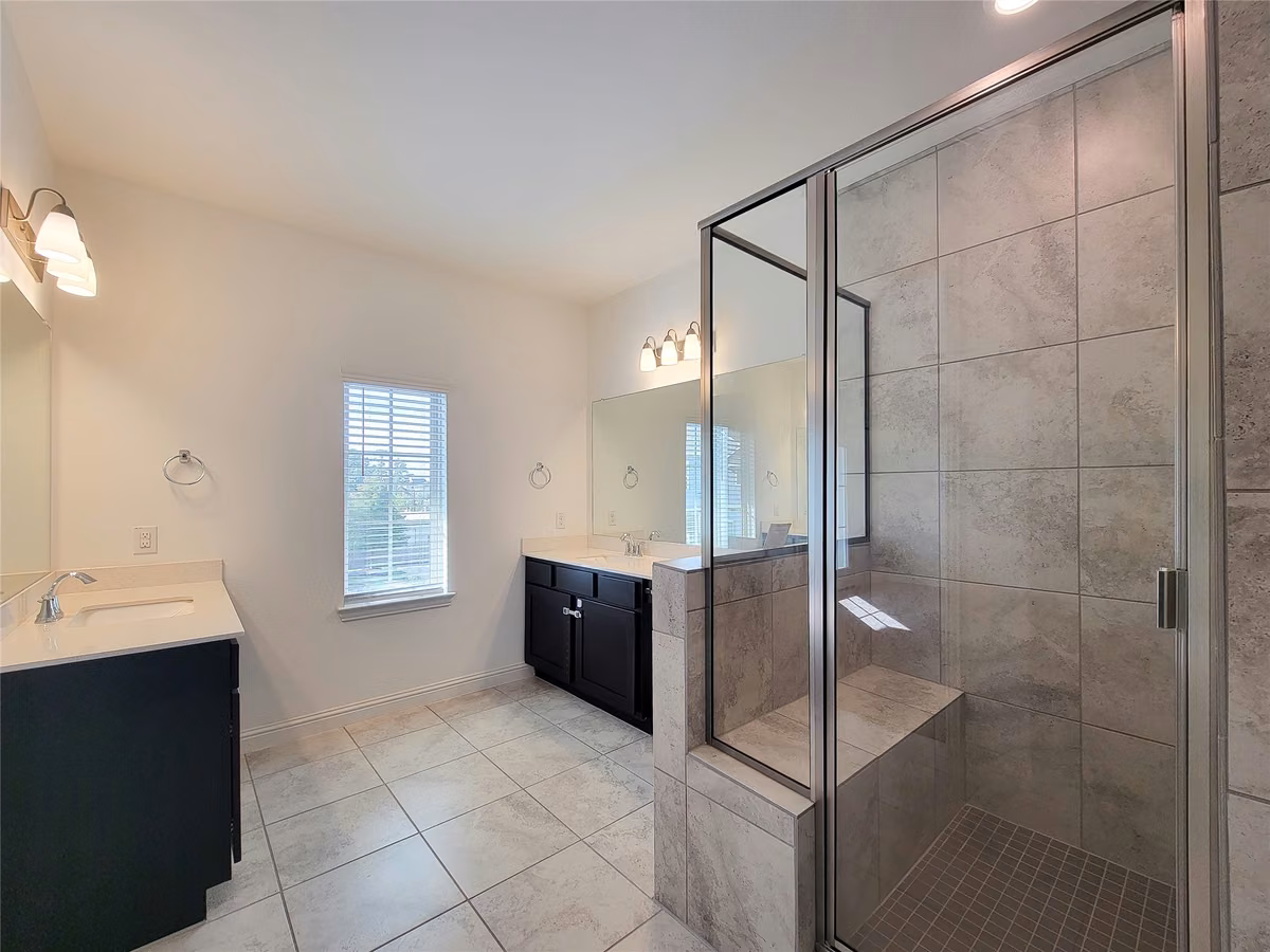 Spacious bathroom featuring a large tiled shower with a glass enclosure, dual vanities, and plenty of natural light.
