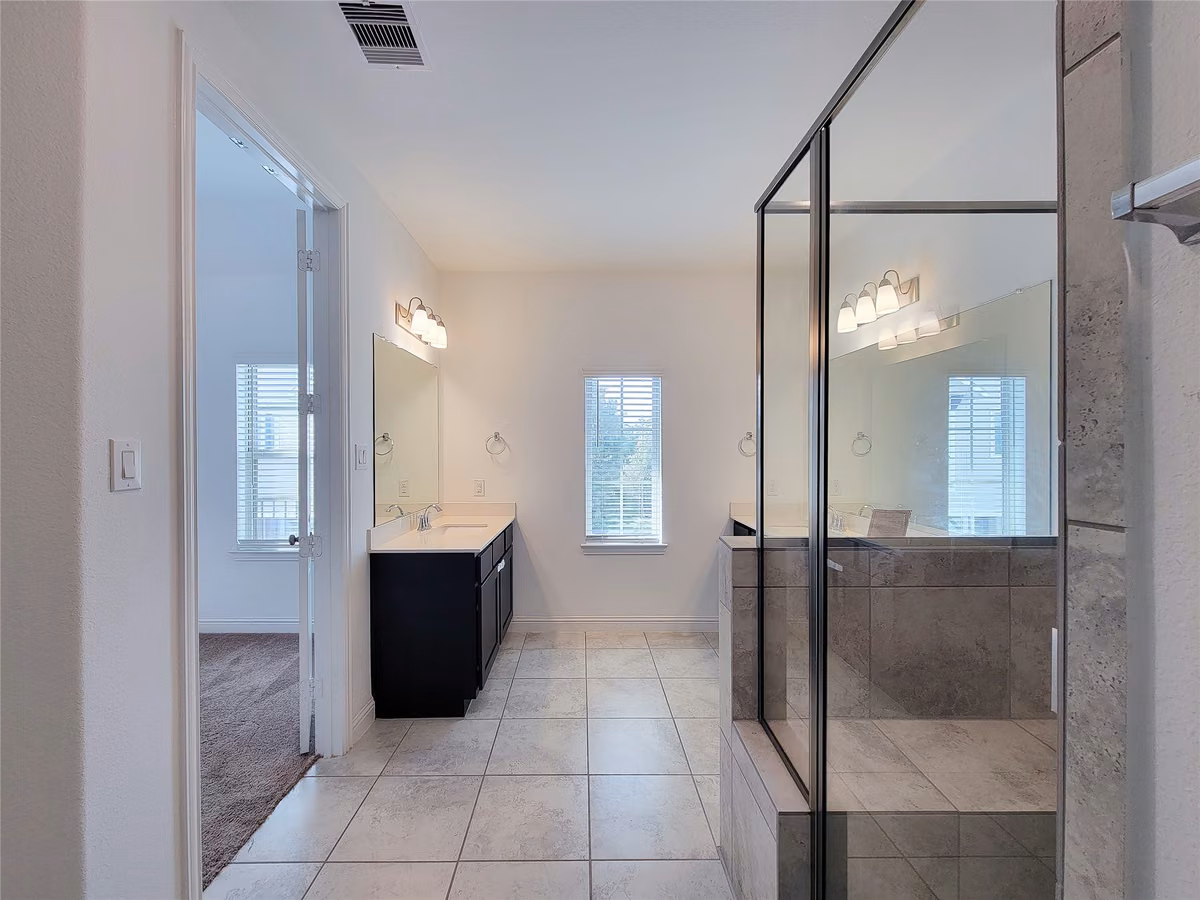 Spacious bathroom features dual sinks, sleek cabinetry, and a large glass-enclosed shower, bathed in natural light from a central window.