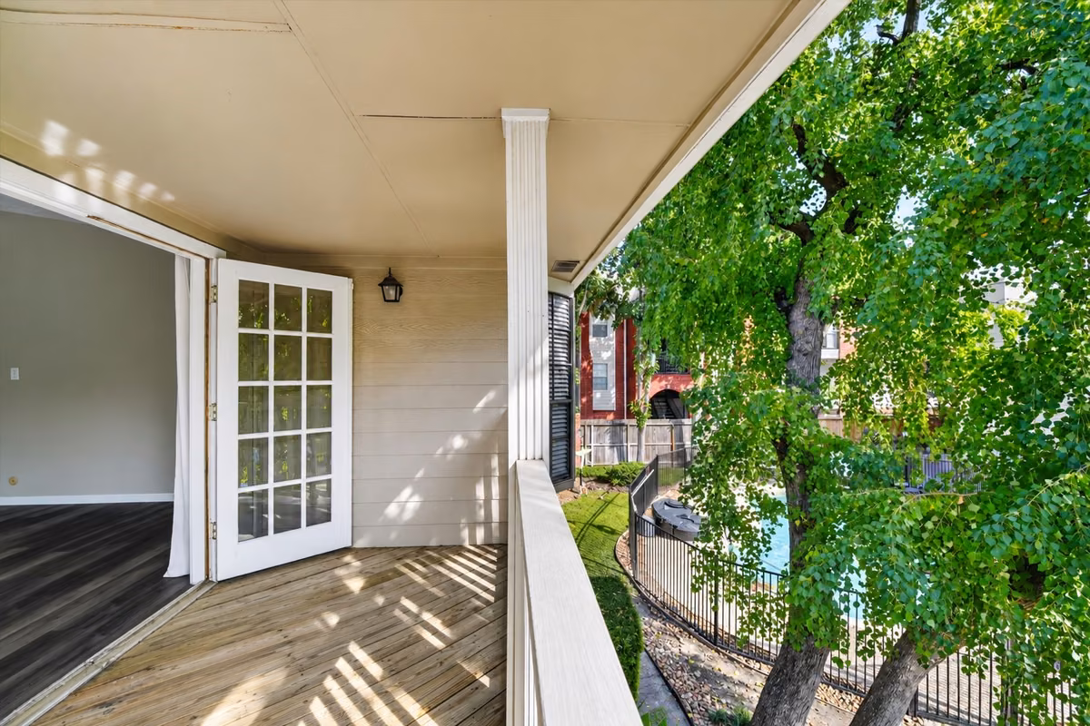 Covered balcony off the primary suite, overlooking mature trees and the community pool—a relaxing retreat for morning coffee or unwinding outdoors.