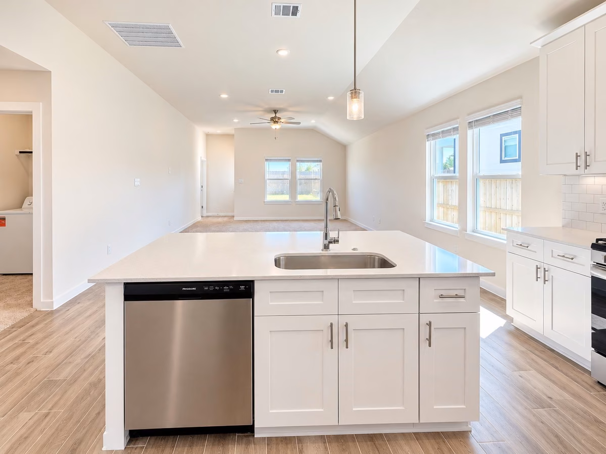 Open-concept kitchen and living area featuring a modern island with a sleek sink, stainless steel appliances, and abundant natural light from large windows.